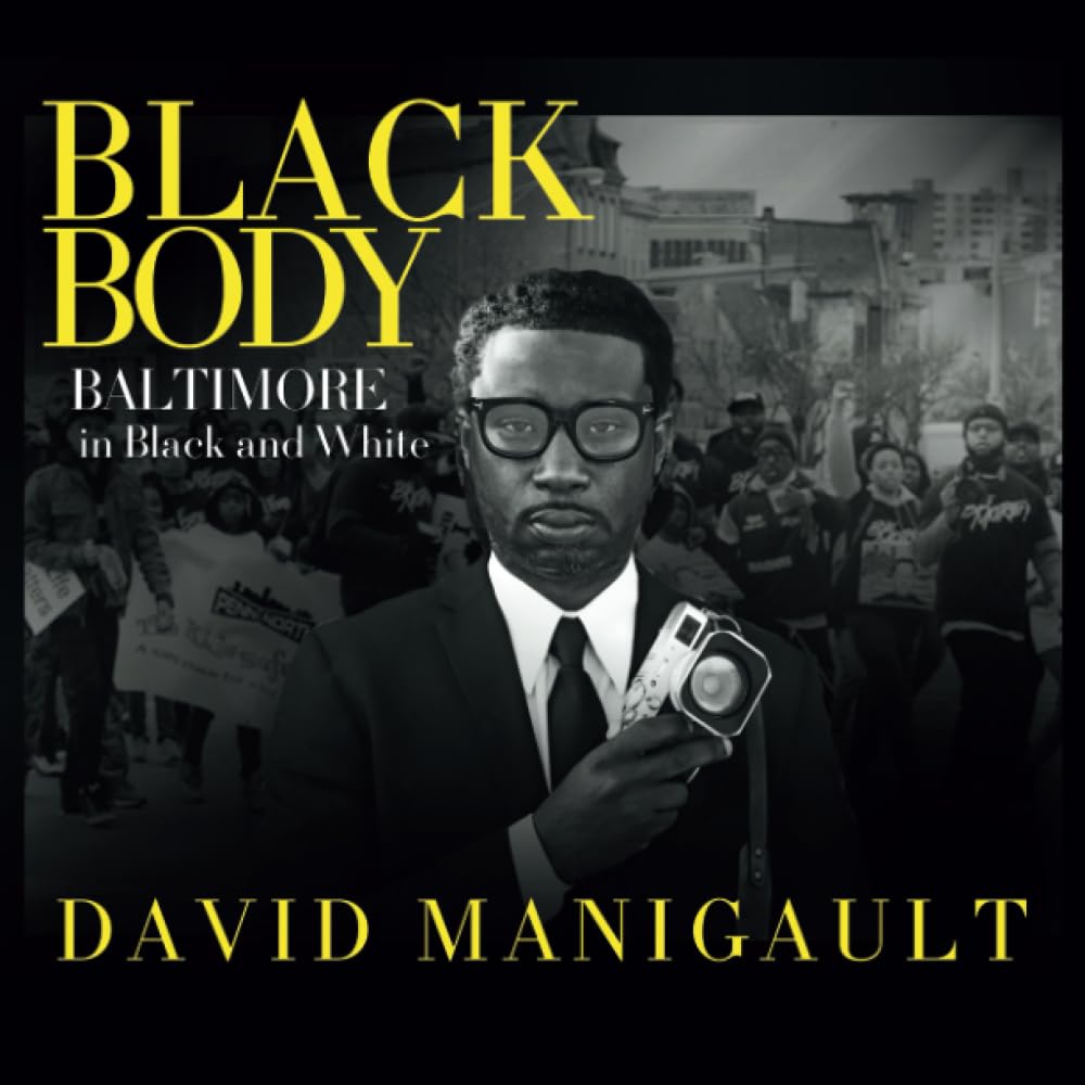 black man in foreground holding camera while city protest happens behind